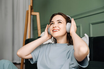 The face of a happy young middle-aged woman wearing wireless headphones, listening to music,...