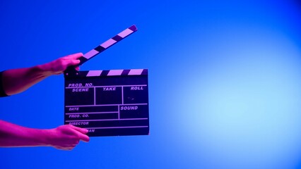 Hand is holding Black clapper board or movie slate on a blue background with a circular light,...