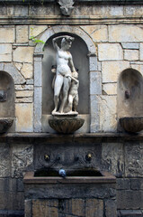 Ancient stone drinking fountain with multiple ornaments and statues in Castelbuono village. Sicily, Italy. Black mold and green moss growing on wet surfaces. Travel and tourism concept