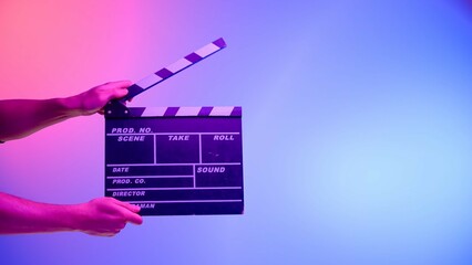 Hand is holding Black clapper board or movie slate on a blue background with a circular light,...