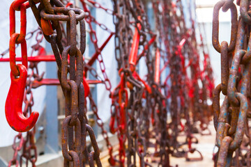 Many rusty red chains with hooks are fastened and hold containers with cargo on the ship.
