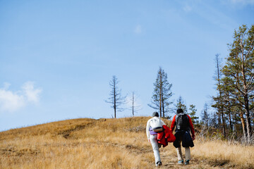 Tourists with backpacks climb the mountain along the slope, spring withered grass, two people walk...