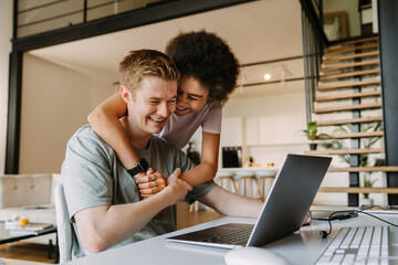 Woman hugging her boyfriend while he working on laptop computer at home - obrazy, fototapety, plakaty