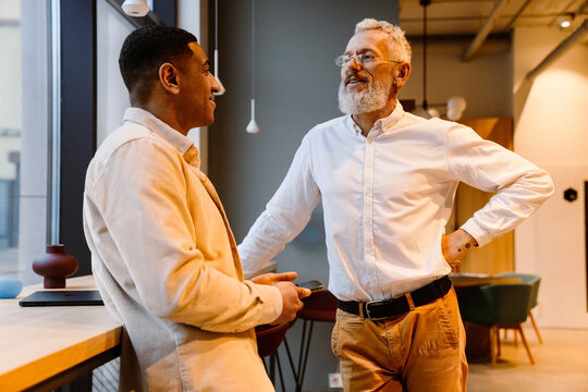 Smiling businessman talking to male colleague while standing in office space - Powered by Adobe