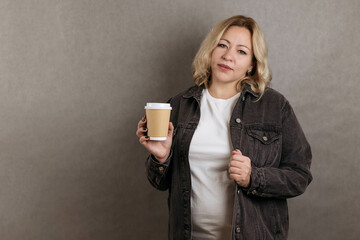 Charming blonde woman size plus size holds two glasses of drinks on a gray background, copy space,...