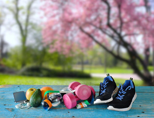 sport and fitness in spring and summer, with sport equipment,waterbottle,dumbbells,measuring tape,smart phone and  fruit. Blurred blooming cherry tree background.