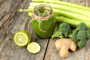 Green vegetable smoothie and green vegetables celery, broccoli, lemon, ginger on a wooden rough...
