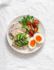 Healthy delicious breakfast on a light background - sandwich with avocado and baked turkey, boiled egg, fresh vegetable salad
