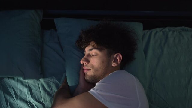 Arab young man sleeping at night in a cozy bed with blue light from the window. Comfortable sleep
