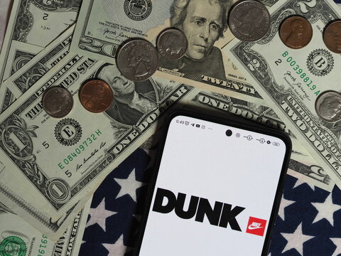 In this photo illustration, a Nike Dunk logo seen displayed on a smartphone with United States Dollar notes and coins in the background. Nike Dunk brand owned by Nike, Inc. corporation