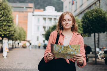 Portrait beautiful blonde woman with paper map in street. Happy tourist travels in Europe. Vacation concept by exploring interesting places to travel. Women Searching locations at summer day.