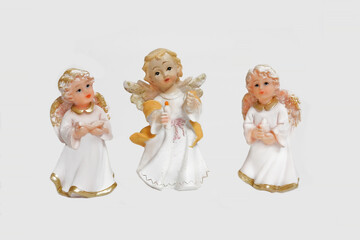 Three porcelain angels in white robes, with gold decoration, pray for the happiness of people. On an isolated background, for cards, illustrations, posters.