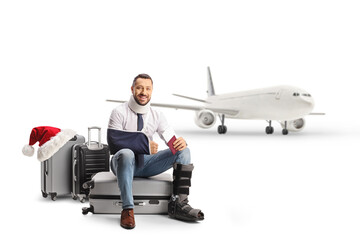 Injured man sitting on a suitcase and holding a passport in front of a plane for a christmas holiday