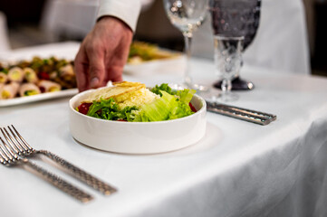 Men's waiter hands hold a Caesar salad with croutons, cheese, eggs, tomatoes and grilled chicken in pub
