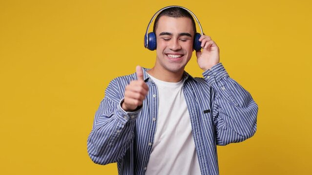 Vivid cheerful calm fun young middle eastern man he wear blue shirt white t-shirt listen mp3 music in headphones slow dance sing song have fun enjoy relax isolated on plain yellow background studio