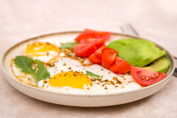 Fried eggs on a plate with avocado and tomatoes. Selective focuse.
