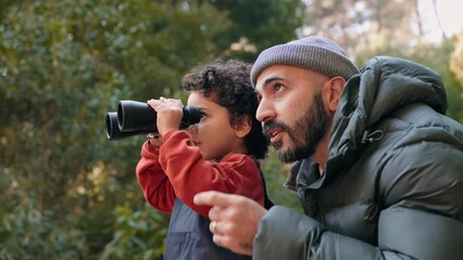 Heartwarming scene of a father and his adorable curly son enjoying nature, looking through binoculars, and sharing laughter in the forest