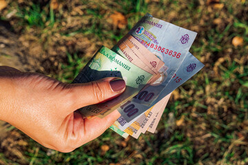 Female hand holding Romanian lei - code RON - money banknotes in denominations of 100, 10 & 1 leu.