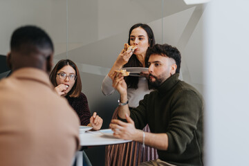 Diverse coworkers on a lunch break, enjoying pizza and relaxing together.