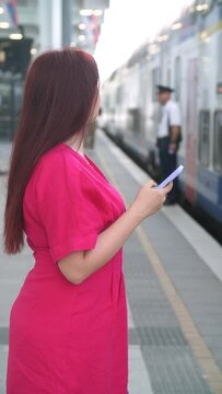 Woman using smart phone while waiting train as arrival. Using Travel App or Checking Train Schedule