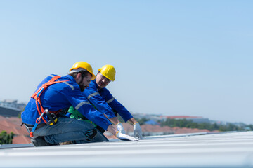 Both of technicians is installing solar panels on the roof of the warehouse to change solar energy into electrical energy for use in factories.