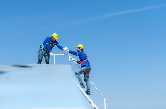 A young technician intern working on solar panels is fear of heights with senior engineers who are always helping out