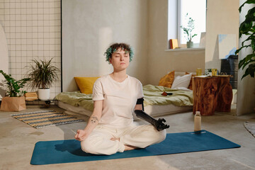 Calm young woman with person with person with disability doing breathing exercise in lotus position