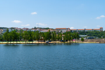 Fototapeta na wymiar A view of the Mondego River and Coimbra City under a clear sky, with trees and buildings. Landscape background and wallpaper.