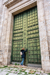 Fototapeta na wymiar Tourist woman knocking on a huge wooden door of the medieval cathedral of Valladolid.