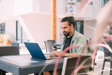 A male freelancer, a digital nomad, remotely works on a laptop in the hotel garden.