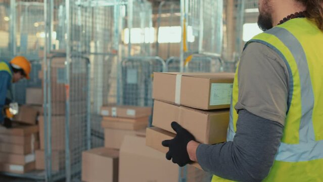 Tracking back shot of unrecognizable warehouse worker carrying goods in cardboard boxes during workday indoors