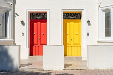 Red and yellow door side by side on white building facade, basking in sunlight