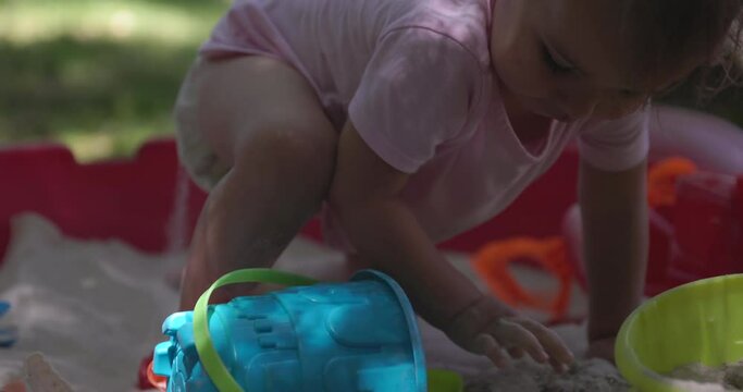 Toddler girl stands up in sandbox covered in sand - slow motion