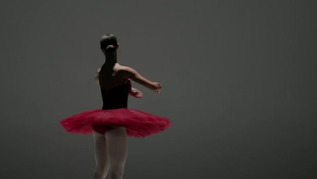 Portrait of female on white background in studio under spotlight. Close up shot ballerina in red tutu and body dancing and spinning around.