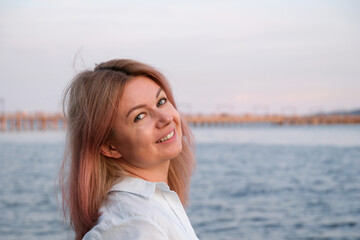 Close-up portrait of a young blonde Caucasian woman with long hair in a black jacket in the city outdoors on a sunny day against the background of the parking lot. Model posing. High quality photo