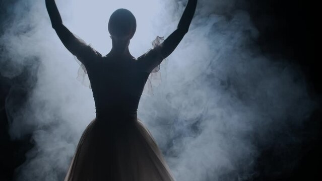 Portrait of female on black background under spotlight projector in studio. Close up shot ballerina in white tulle dancing around in smoke.