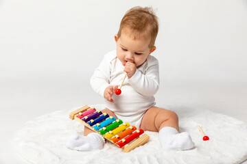 Smiling toddler newborn girl playing on wooden xylophone. Cute little child in white suit enjoying...