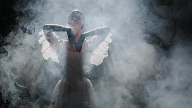 Portrait of female on black background under spotlight projector in studio. Close up shot ballerina in white tulle dancing posing in smoke.