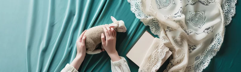 Foto op Plexiglas Delicate hands comforting a lamb on satin teal fabric, accompanied by a vintage lace dress and an open book © Breezze