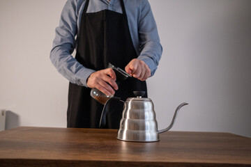 Barista man grinding coffee beans with a manual coffee grinder in his hand