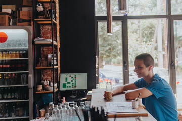 A teenager enjoying coffee at a cafe bar, browsing the internet on his smart phone after school. He seems happy and relaxed, chatting with friends and checking social media. - obrazy, fototapety, plakaty