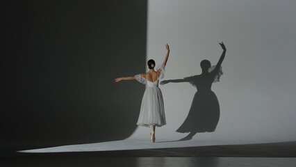 Portrait of female on white background in studio under spotlight. Beautiful ballerina in white tulle dancing slow element of choreography. © kinomaster