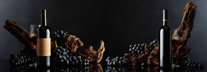 Bottles of red wine with old weathered snag and blue grapes. - obrazy, fototapety, plakaty