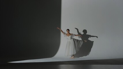 Female on white background in studio under spotlight. Beautiful ballerina in white tulle dancing...