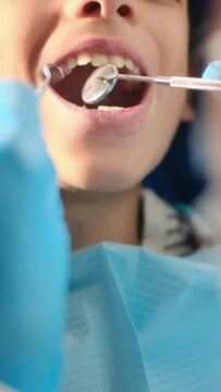 While assessing a young patient for tooth decay, a compassionate female dentist employs a dental probe and angled mirror.