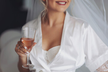 smiling bride in silk robe holding champagne flute. Girl in a white bathrobe with a wedding ring on...