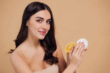 Beauty portrait of happy woman holding fruit and bank of cream on beige background