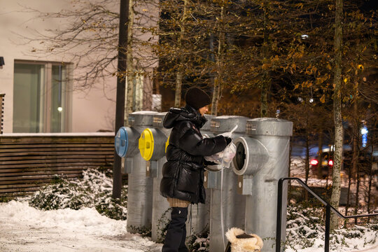 Stockholm, Sweden, A young woman throws garbage in a shute with a dog on a leash in a resdiential complex at night in the winter.