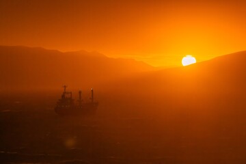The hour of dawn over the Black Sea near the city of Novorossiysk - the sun, orange light and a large ship in the roadstead