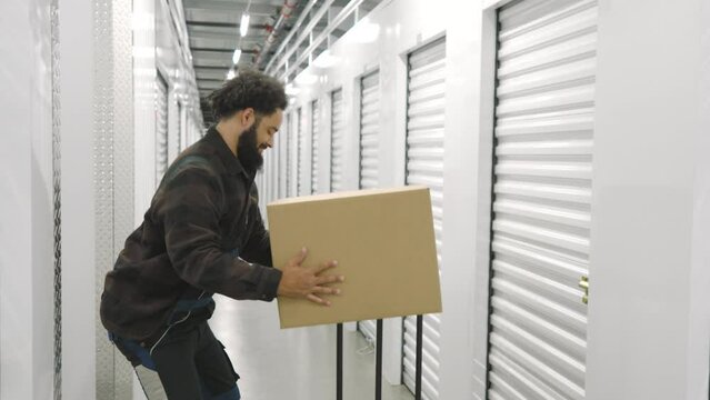 African American in work overalls lifting heavy boxes with items of customer, employee touching lower back feeling pain. Loader in self storage company. High quality 4k footage